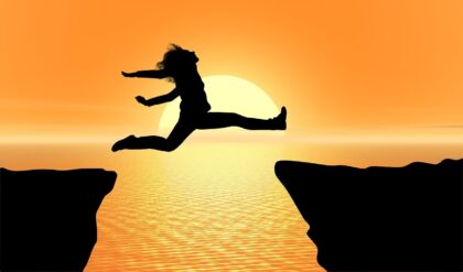 Silhouette of a person leaping from one rock to another, at sunset